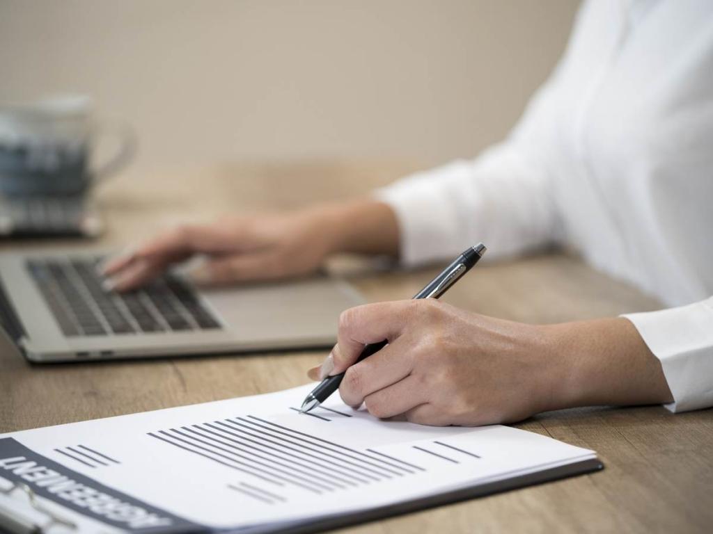 Person working at a laptop while checking a clipboard.